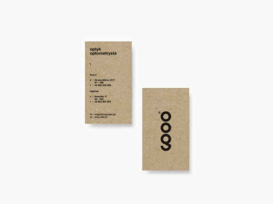 The image shows two business cards.  Both are printed on light brown, textured card stock that resembles recycled paper. One card displays contact information for an optician/optometrist in Polish (optyk optometrysta), including addresses and phone numbers for two locations (Bydgoszcz and Gdańsk). The other card features a simple logo – a stylized vertical arrangement of four overlapping circles.  The overall aesthetic is minimalist and eco-friendly.